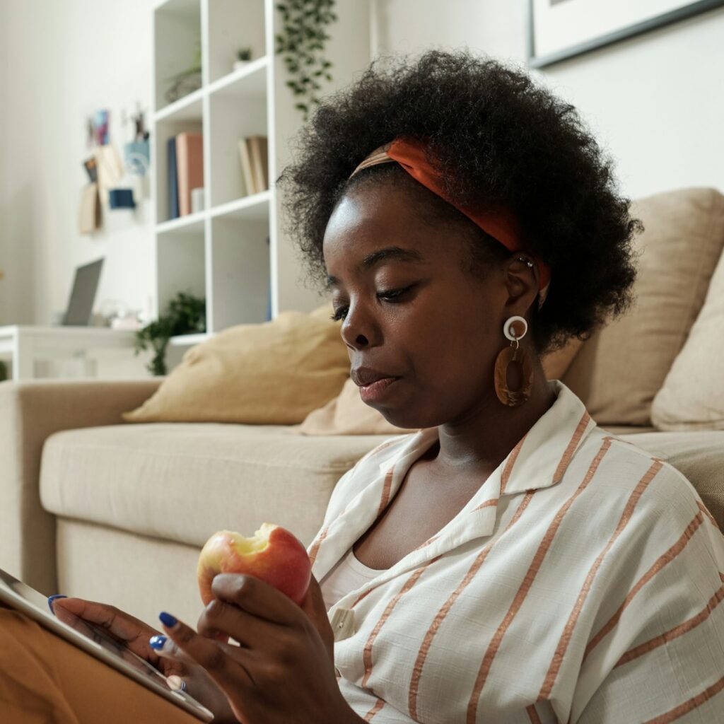 Busy young African freelancer with apple scrolling in tablet