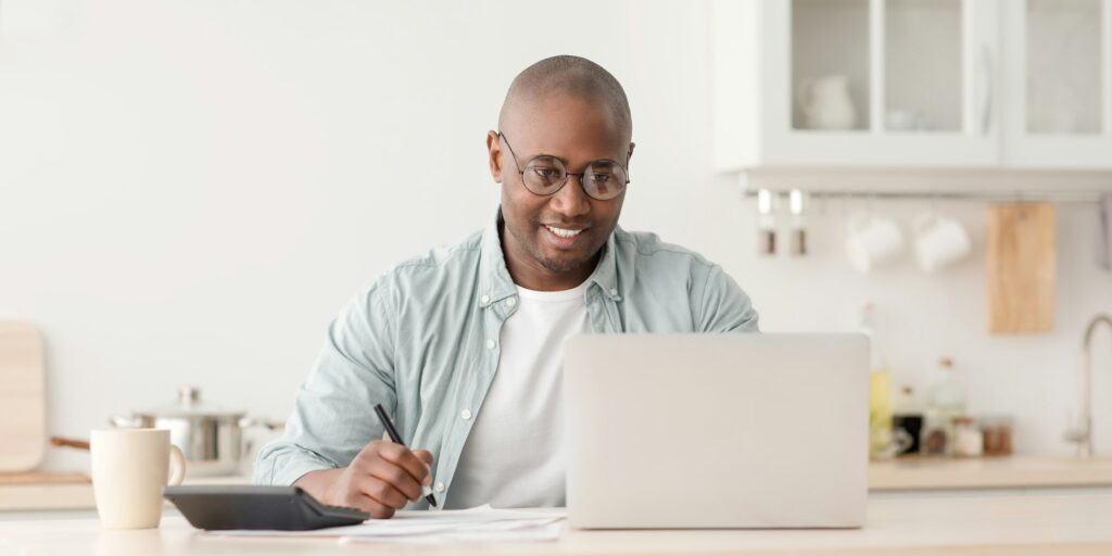 Plan finances. Positive african american mature man calculating taxes and using laptop computer