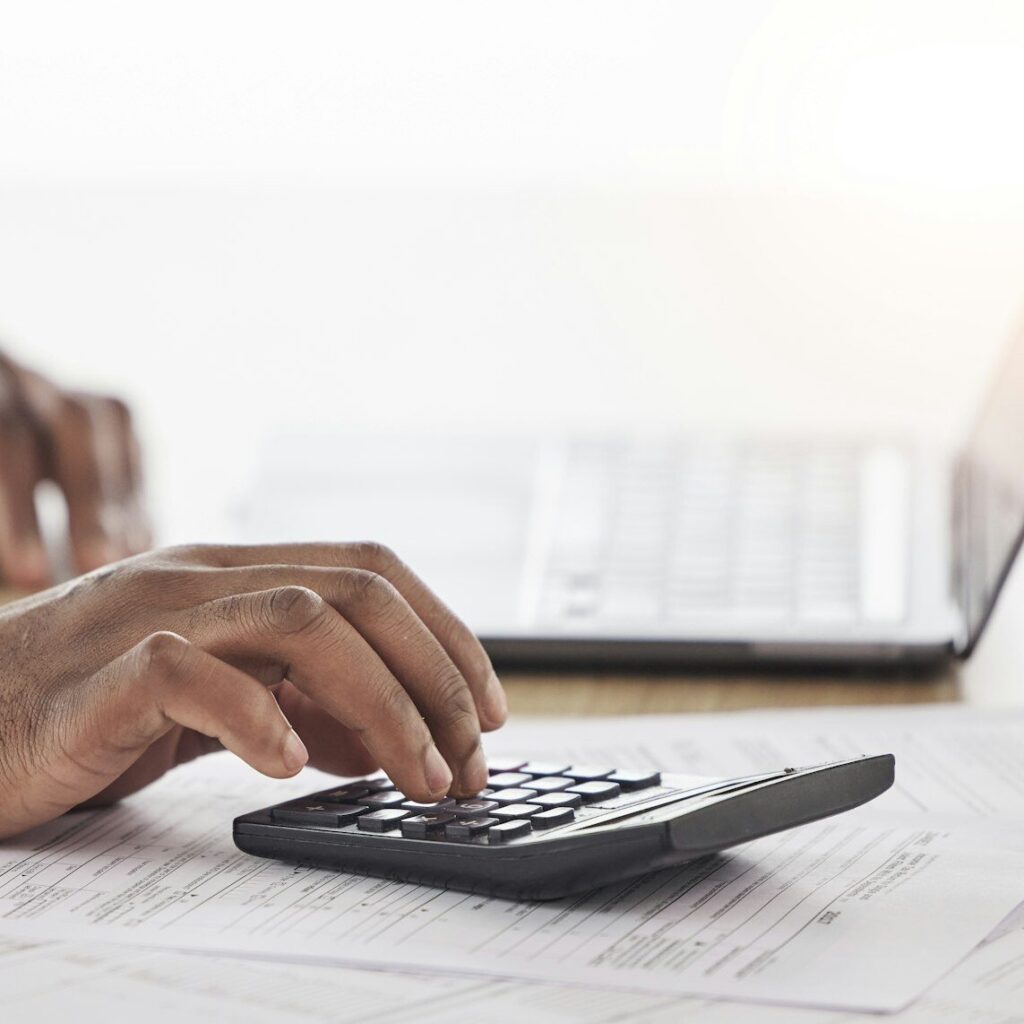 Hand using a calculator next to a laptop for bookkeeping – Zidika Consulting, Kenya