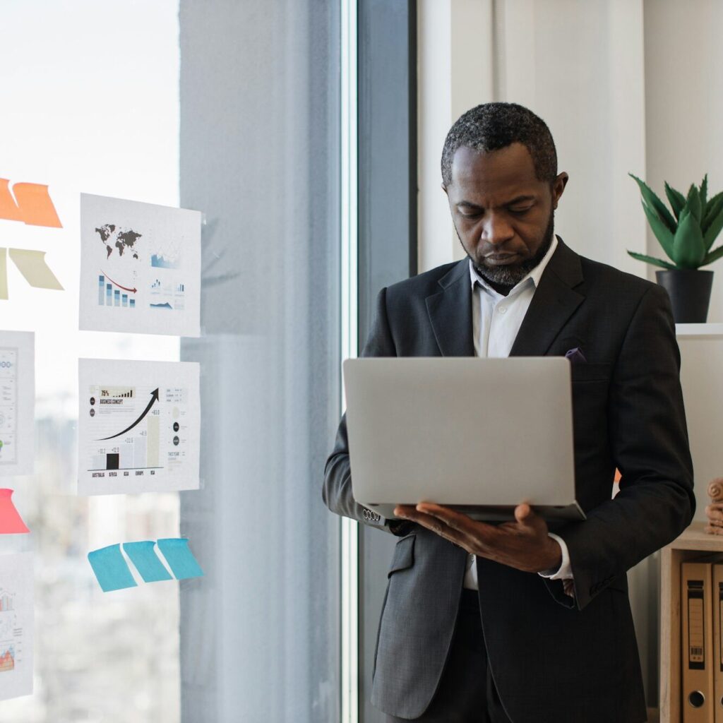 Businessman presenting with laptop beside glass board – Zidika Consulting