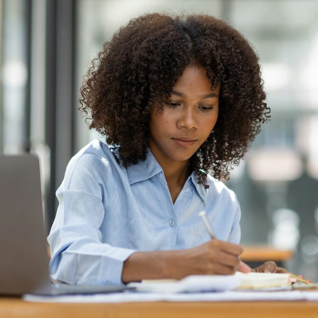 Woman in Nairobi writing in a notebook next to her laptop for tax tracking – Zidika Consulting